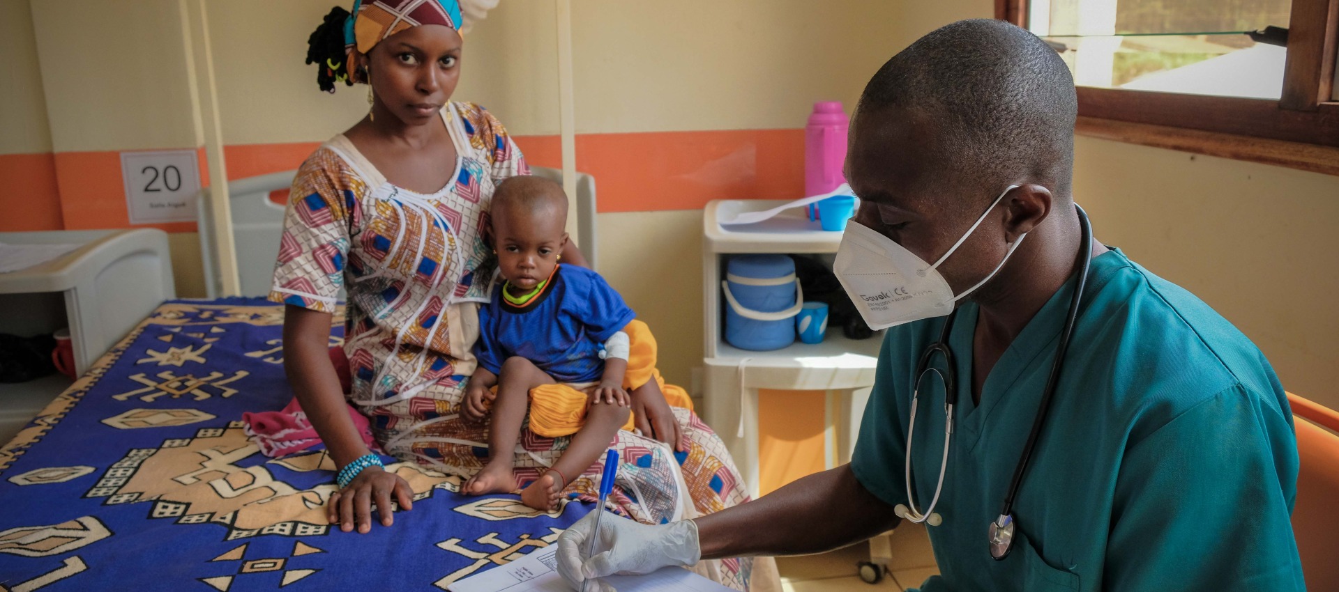 A healthcare worker in a mask with a mother and child at the pediatric hospital in Bangui, Central African Republic.