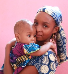 A mother and child in front of a pink wall in Cameroon.