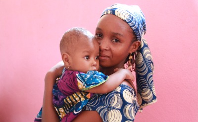 A mother and child in front of a pink wall in Cameroon.