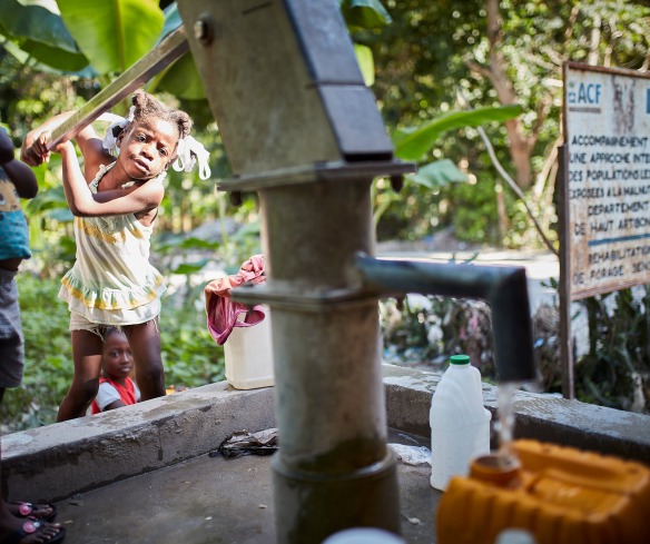 A young girl pumps water from a pump built by Action Against Hunger in 2008. Reliable access to clean water, safe sanitation, and good hygiene remains a challenge in Haiti.