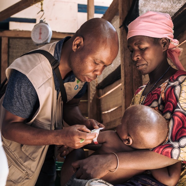 A health worker checks the nutrition status of a young boy as his mother holds him.
