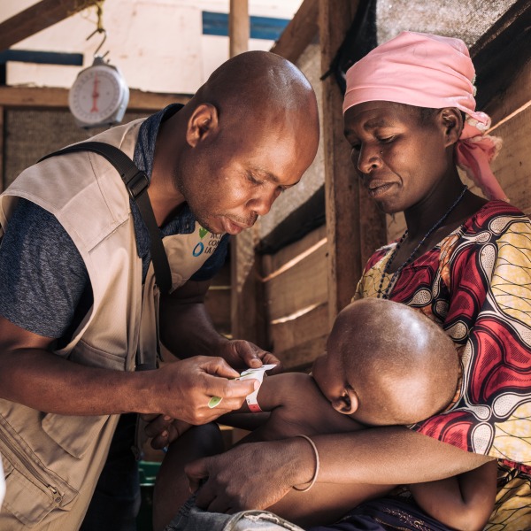 A health worker checks the nutrition status of a young boy as his mother holds him.