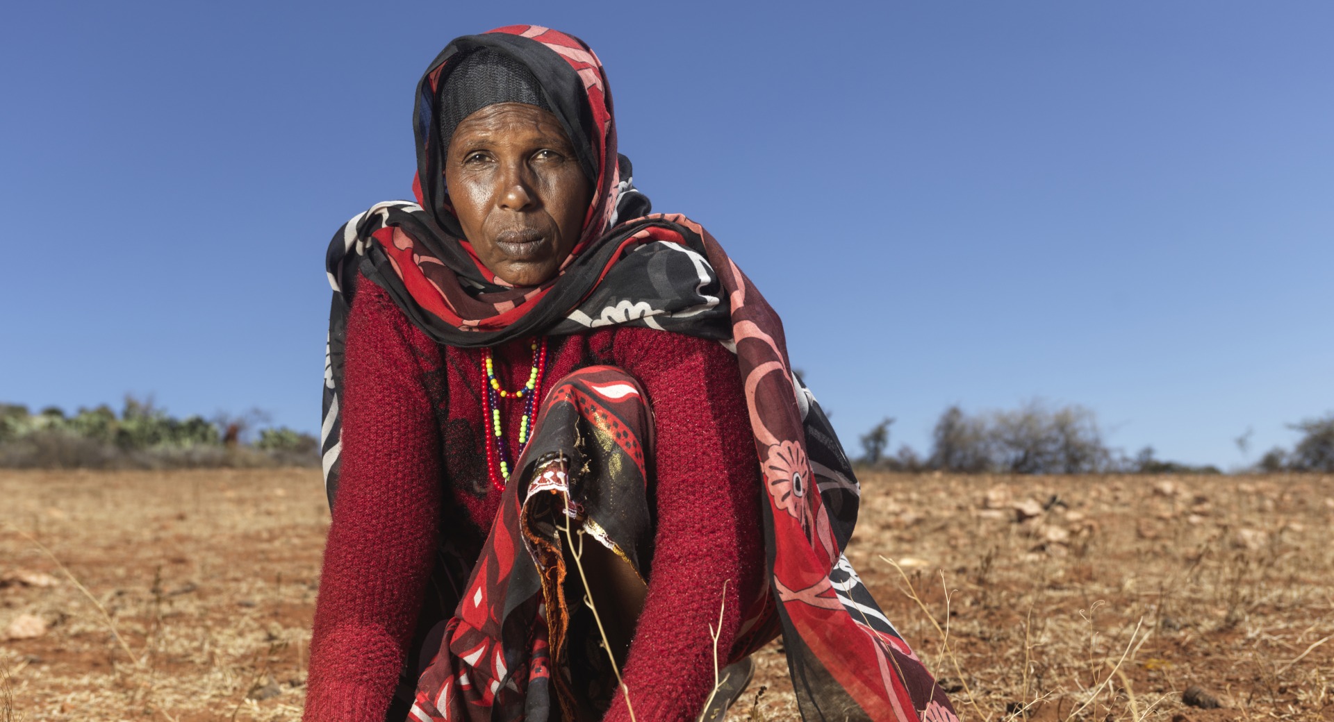 A woman kneels in her fields, which have been dried up and devastated by drought.