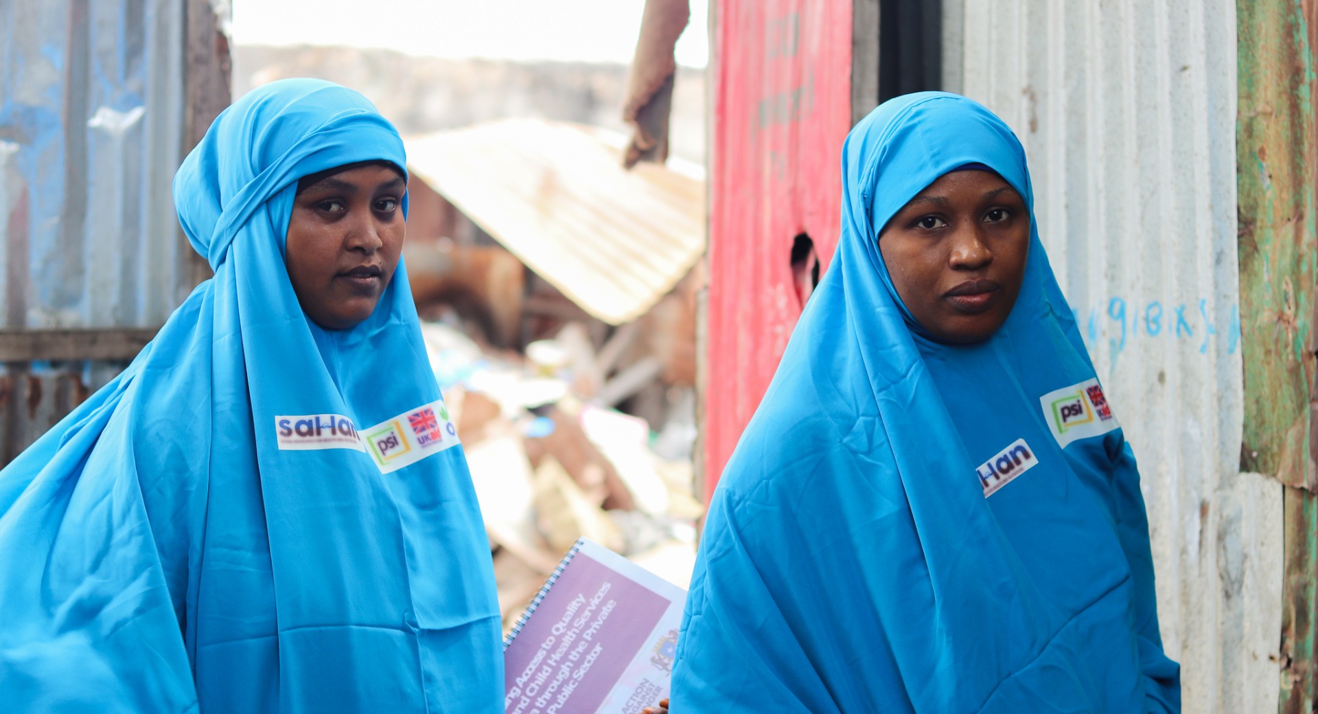 Two Female Community Influencers, Fardosa (left) and Amina (right), pose before they head into a home to meet with a mother.