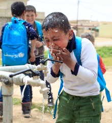 A boy splashes water on his face at a tap installed by Action Against Hunger.