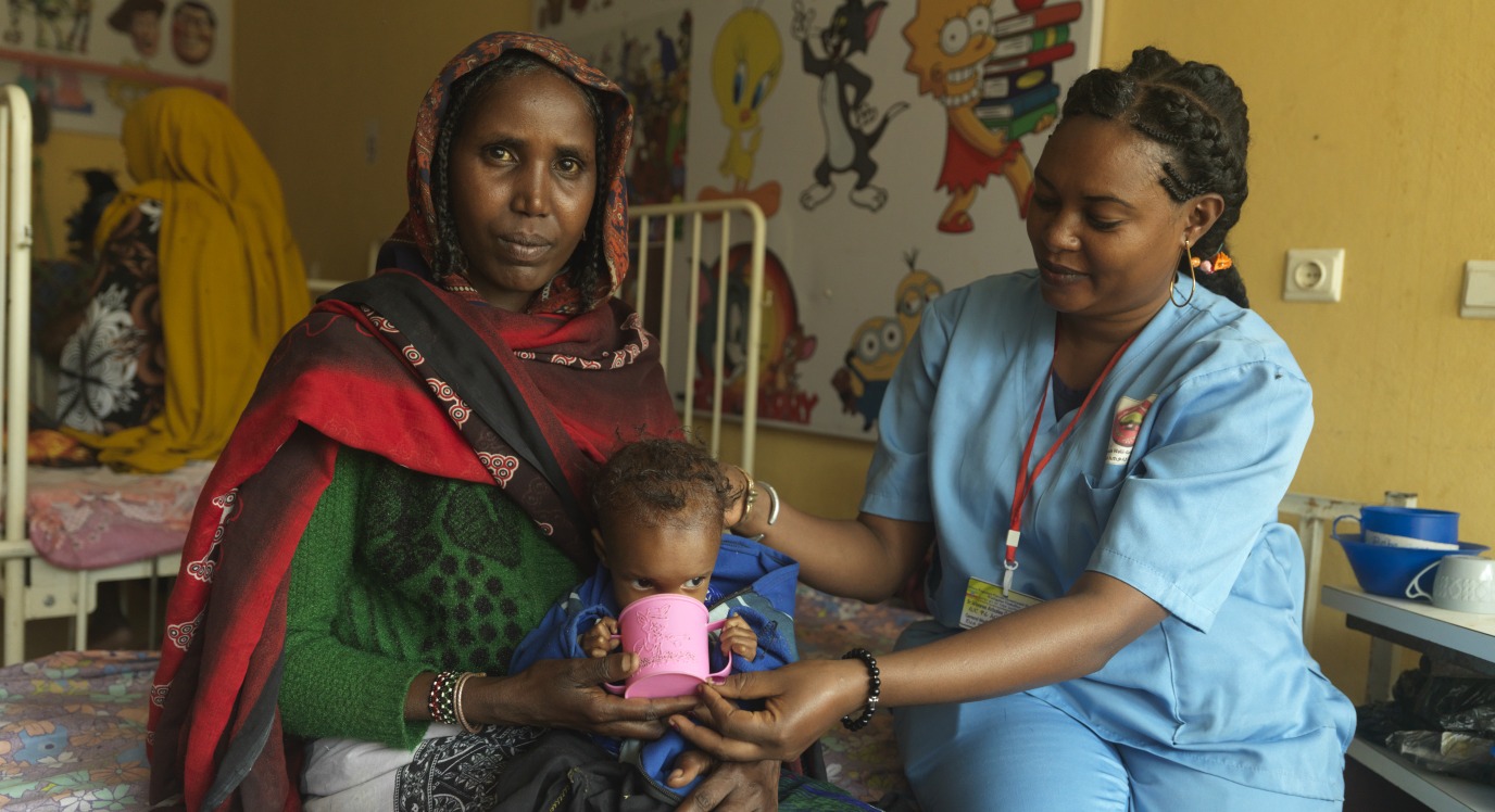 At the Stabilization Center at Yabelo General Hospital in Ethiopia, Nurse Ware helps severely malnourished Dabo drink therapeutic milk as treatment for Dabo's malnutrition.