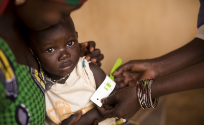 A health worker measures a child's upper arm with a color-coded band that is used to detect malnutrition.