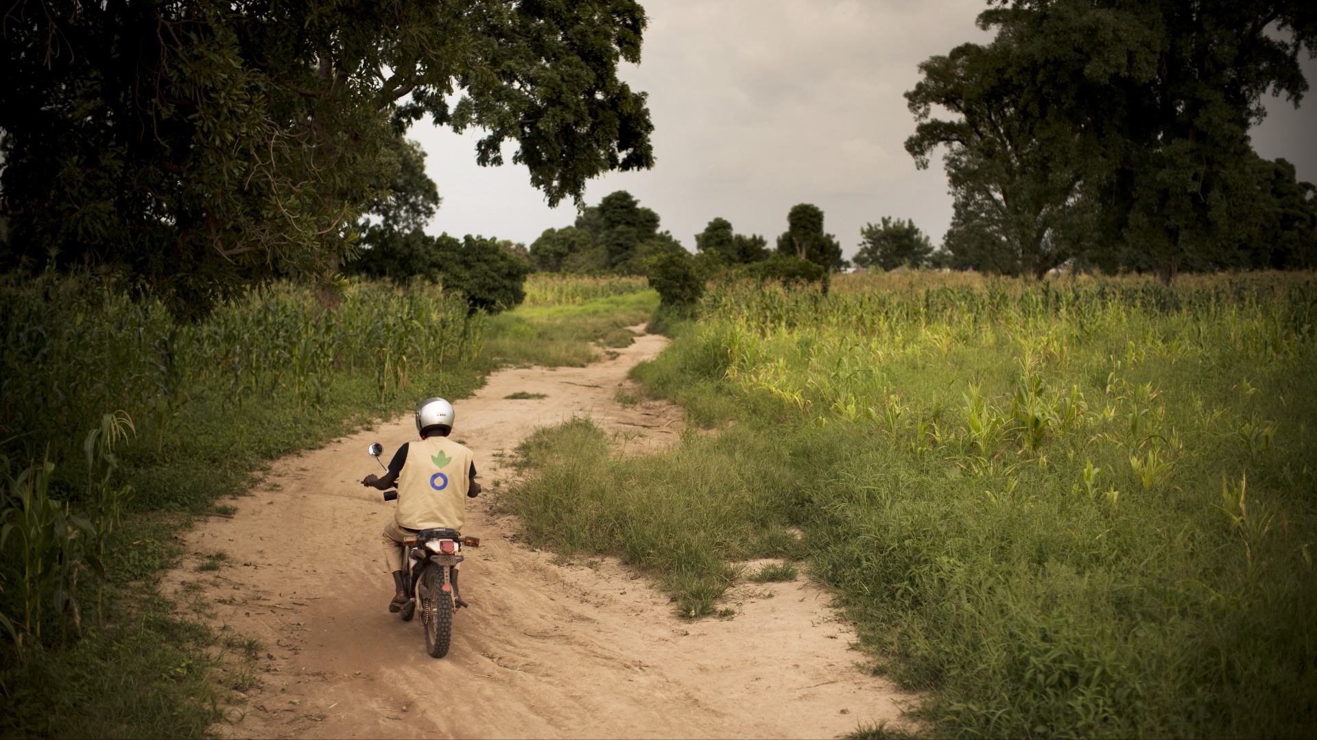 An Action Against Hunger aid worker drives a motorbike down a dirt road in Mali