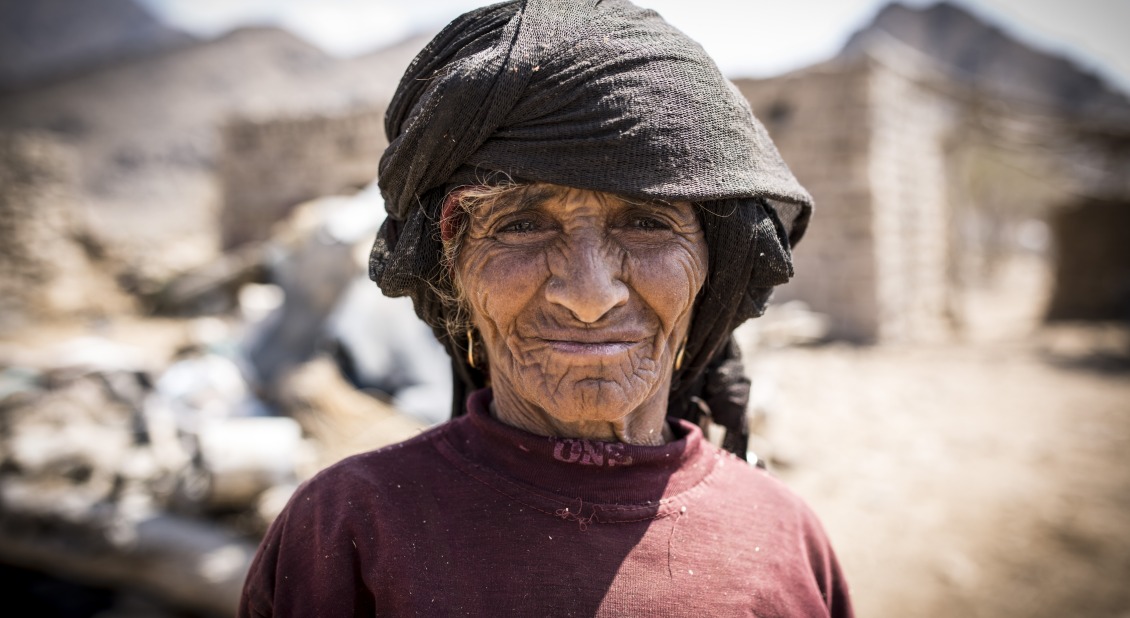 In Yemen, a woman stands in front of her community, which has been destroyed by conflict.