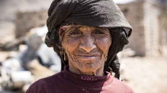 In Yemen, a woman stands in front of her community, which has been destroyed by conflict.